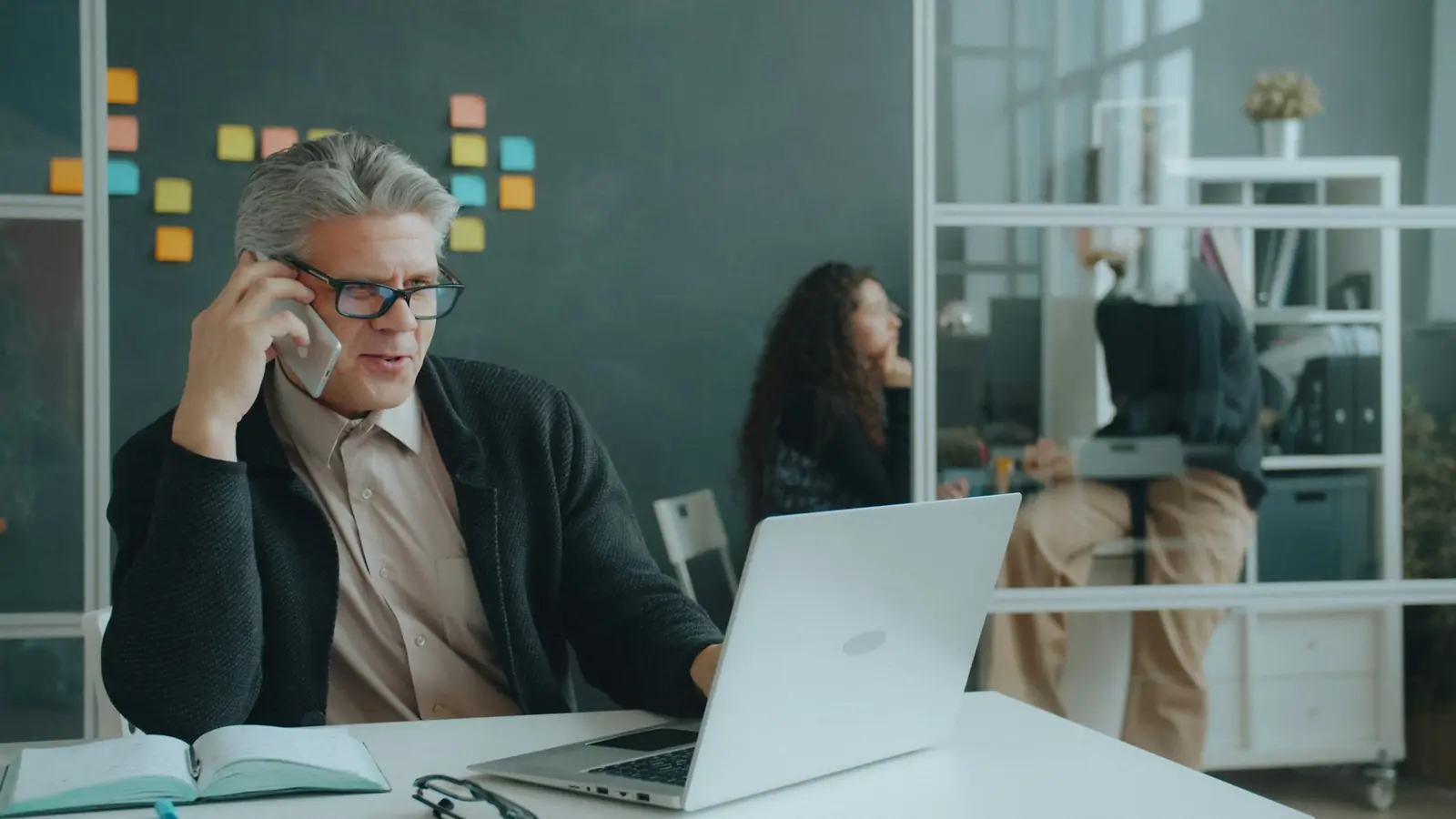 Ein Mann mit Brille telefoniert am Schreibtisch und schaut dabei auf seinen Laptop.