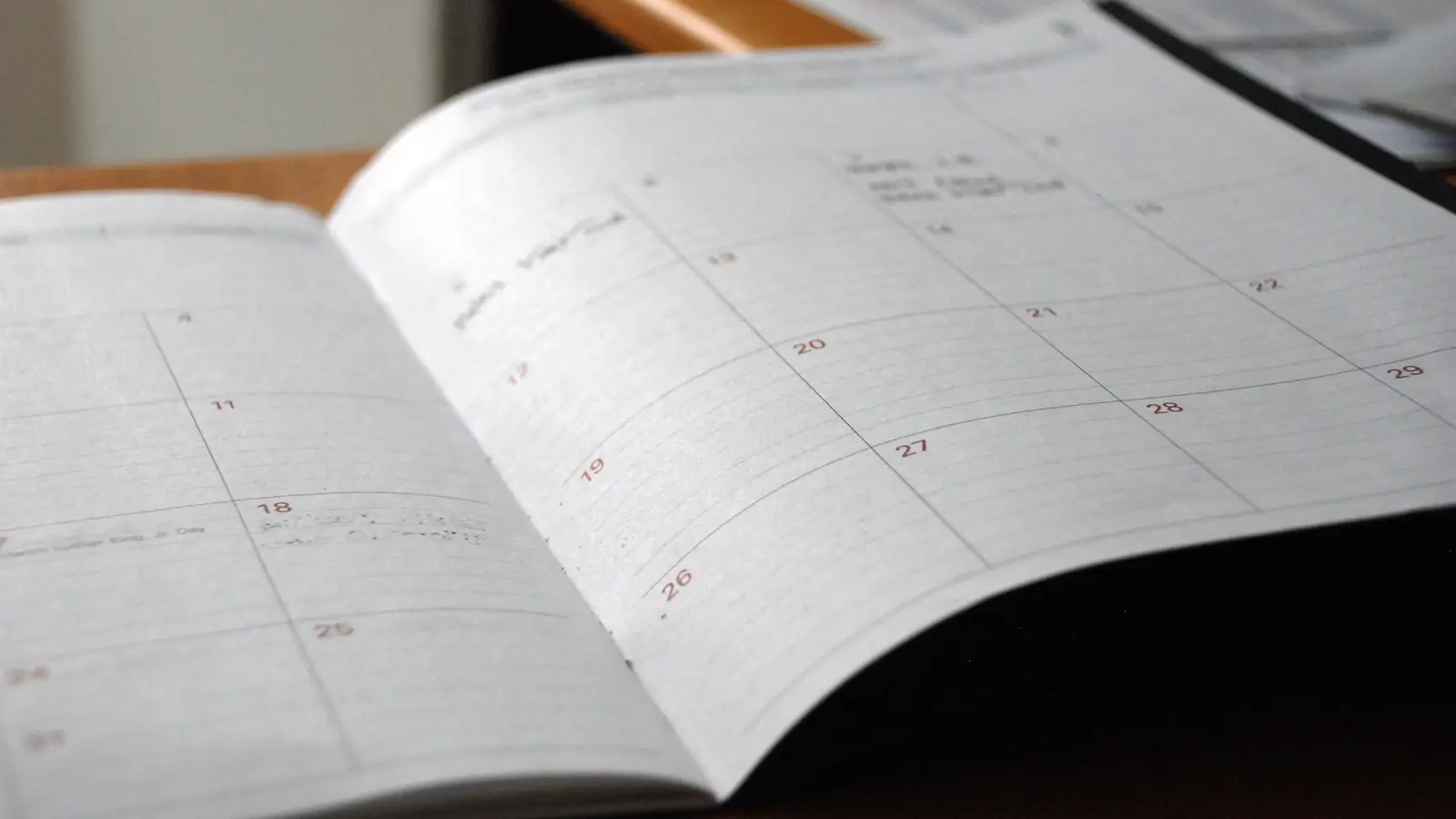 Ein aufgeschlagener Monatskalender mit einzelnen handschriftlichen Einträgen liegt auf einem Tisch.