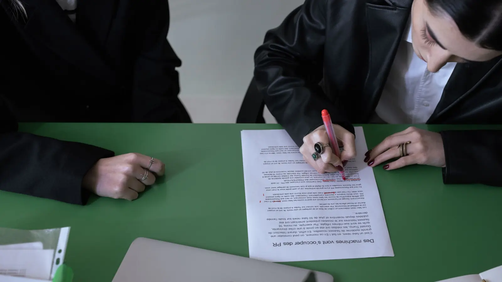 Eine Hand markiert mit einem roten Stift Stellen in einem ausgedruckten Textentwurf auf einem grünen Tisch.