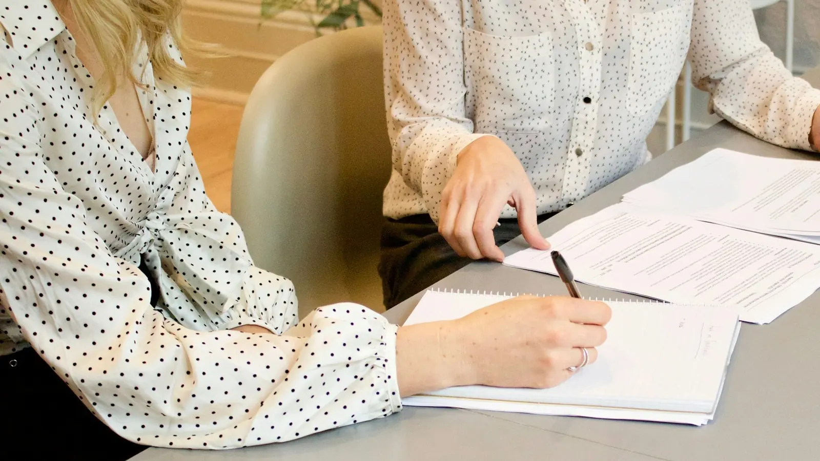Zwei Frauen gehen an einem Tisch Vertragsunterlagen durch, eine macht sich Notizen.