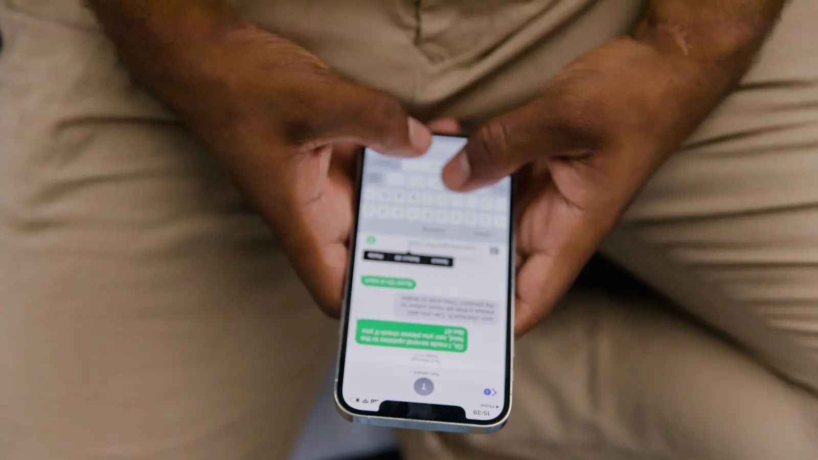 Eine Person hält ein Smartphone mit einem geöffneten Nachrichtenverlauf in beiden Händen.